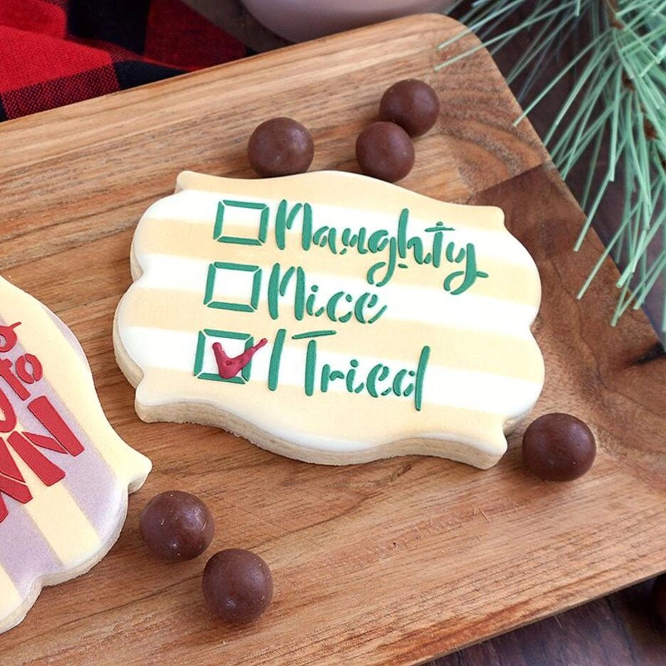 Sfeerbeeld van een kerstkoekje gedecoreerd met The Cookie Countess Naughty Nice I Tried stencil, grappige checklist met Naughty, Nice en I Tried aangevinkt in groen en rood op een gestreept koekje, gepresenteerd op een houten plank met chocolade kerstballen