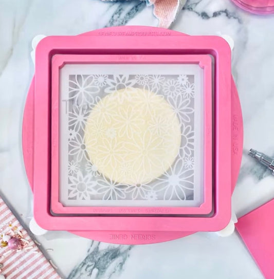 Roze Screen Genie van de Creative Cookier met fijn gaas over een bloemenstencil op een rond koekje