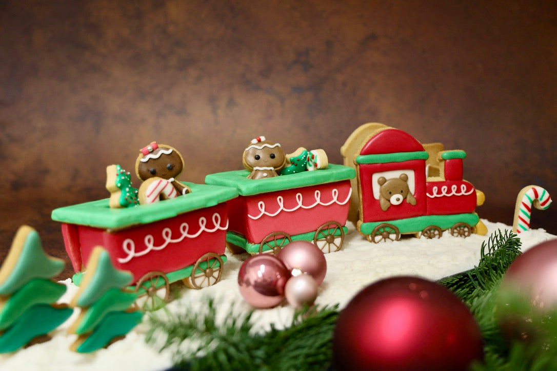 Kersttrein van koekjes met een gespoten beertje in de locomotief en twee wagons met gingerbread koekjes tussen kerstballen