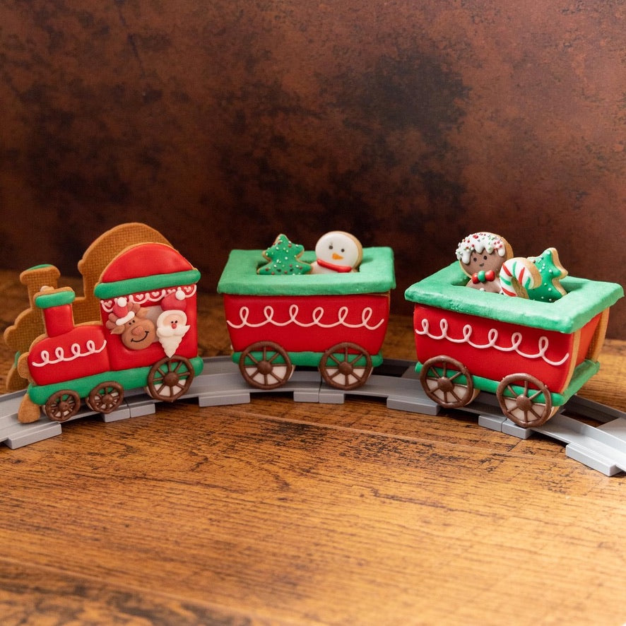 3D trein van koekjes als kersttrein: rode locomotief met kerstman en rendier en twee wagons met kleine kerstkoekjes op rails
