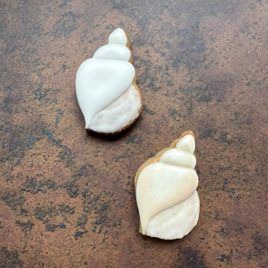 Twee wulk schelp koekjes van de Wulk 2 uitsteker: links met witte royal icing, rechts geverfd met verdunde kleurstof voor diepte op de naden