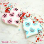 Sfeerbeeld van gedecoreerde hartkoekjes met The Cookie Countess 2 Part Conversation Hearts stencil, kleurrijke hartjes met lieve teksten in roze, blauw en wit, perfect voor Valentijnsdag koekjes