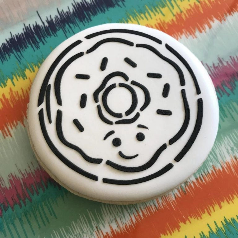 Rond koekje met The Cookie Countess Donut PYO (Paint Your Own) stencil patroon, een donut ontwerp klaar om in te kleuren met eetbare verf op een kleurrijke achtergrond