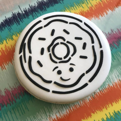 Rond koekje met The Cookie Countess Donut PYO (Paint Your Own) stencil patroon, een donut ontwerp klaar om in te kleuren met eetbare verf op een kleurrijke achtergrond