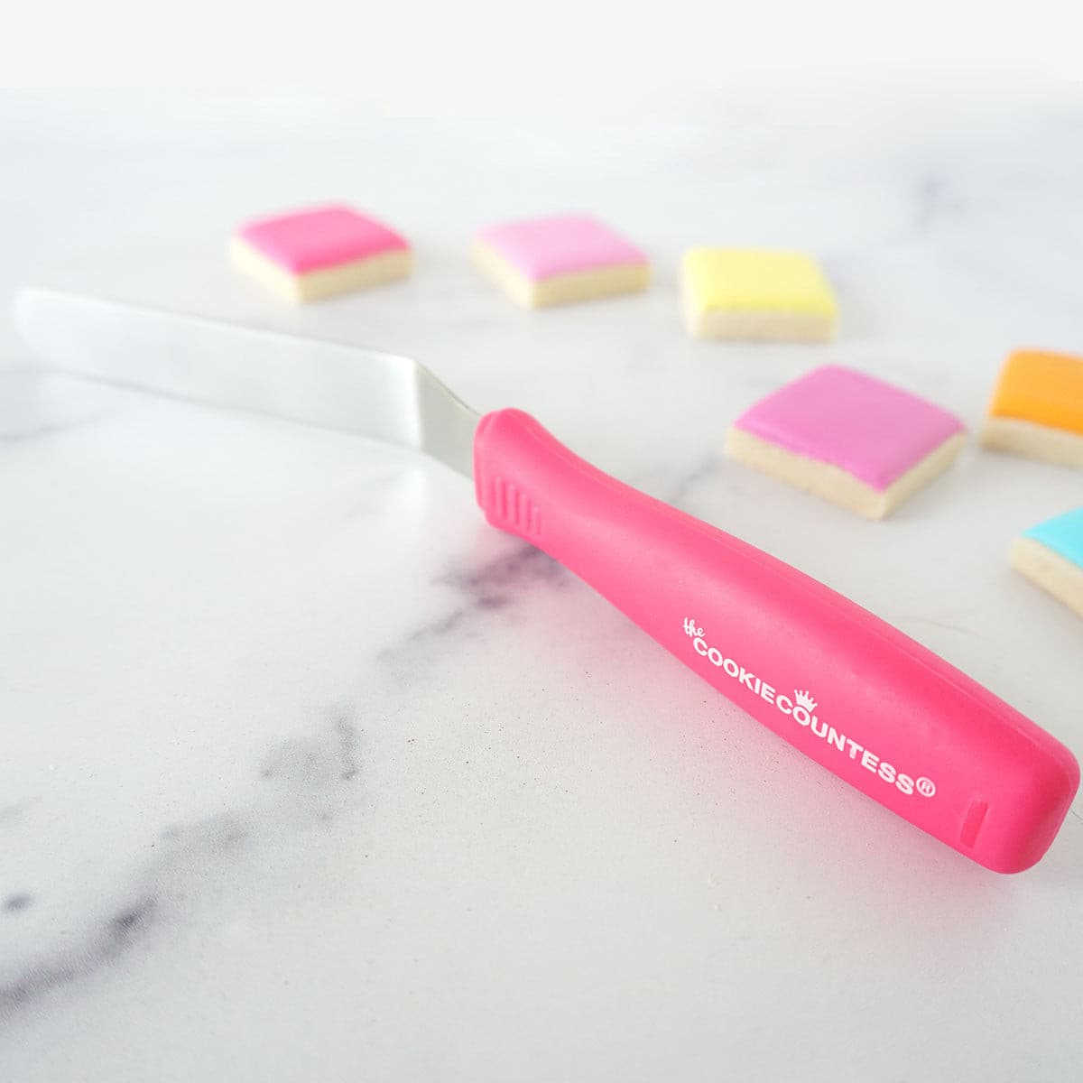 Roze mini offset spatel van The Cookie Countess tussen gedecoreerde koekjes