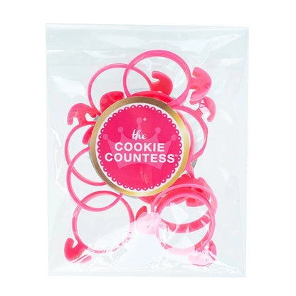 The Cookie Countess Piping Bag Ties verpakking met roze spuitzakclips in een transparant zakje met The Cookie Countess logo sticker, handige herbruikbare clips voor het afsluiten van spuitzakken bij het decoreren van koekjes