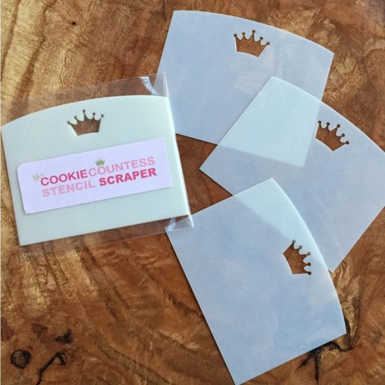 The Cookie Countess Stencil Scraper 3-pack met drie witte kunststof scrapers met kroon logo op houten ondergrond, inclusief verpakking, onmisbaar hulpmiddel voor het strak aanbrengen van royal icing bij koekjes decoreren