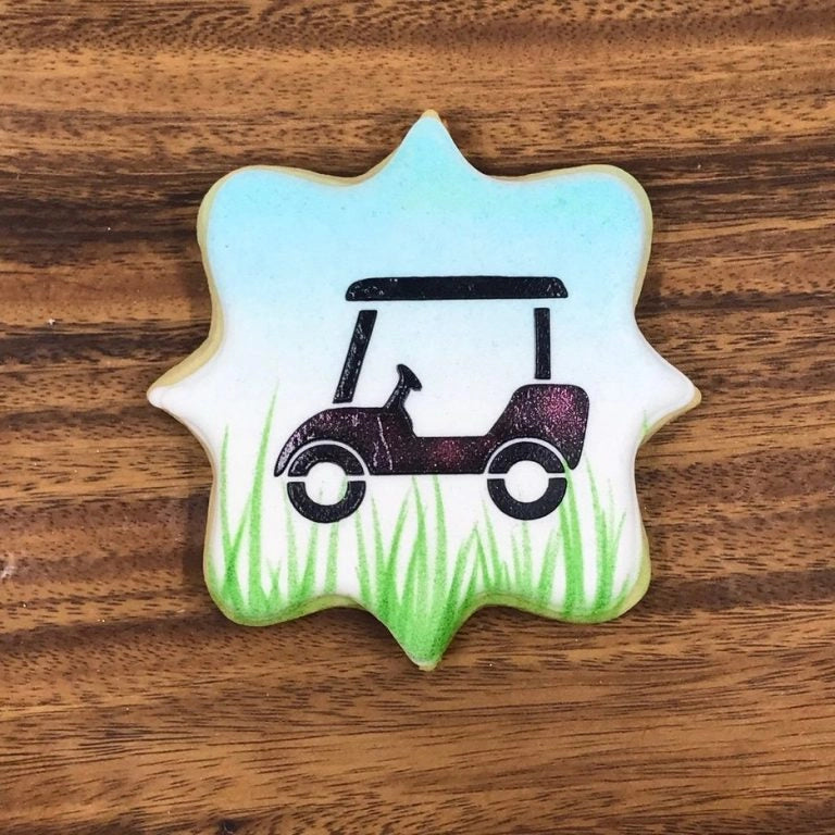 Versierd koekje met The Cookie Countess Tall Grass stencil patroon, golfkarretje met hoog gras op een blauw-wit koekje, ideaal voorbeeld van airbrush decoratie