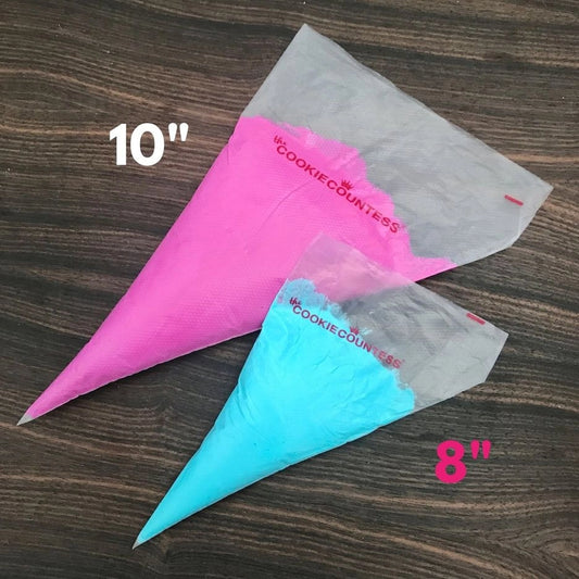 The Cookie Countess Tipless Piping Bags in twee maten, roze 10 inch en blauw 8 inch spuitzakken zonder spuitmond op een houten ondergrond, herbruikbare siliconen spuitzakken voor het decoreren van koekjes en cupcakes