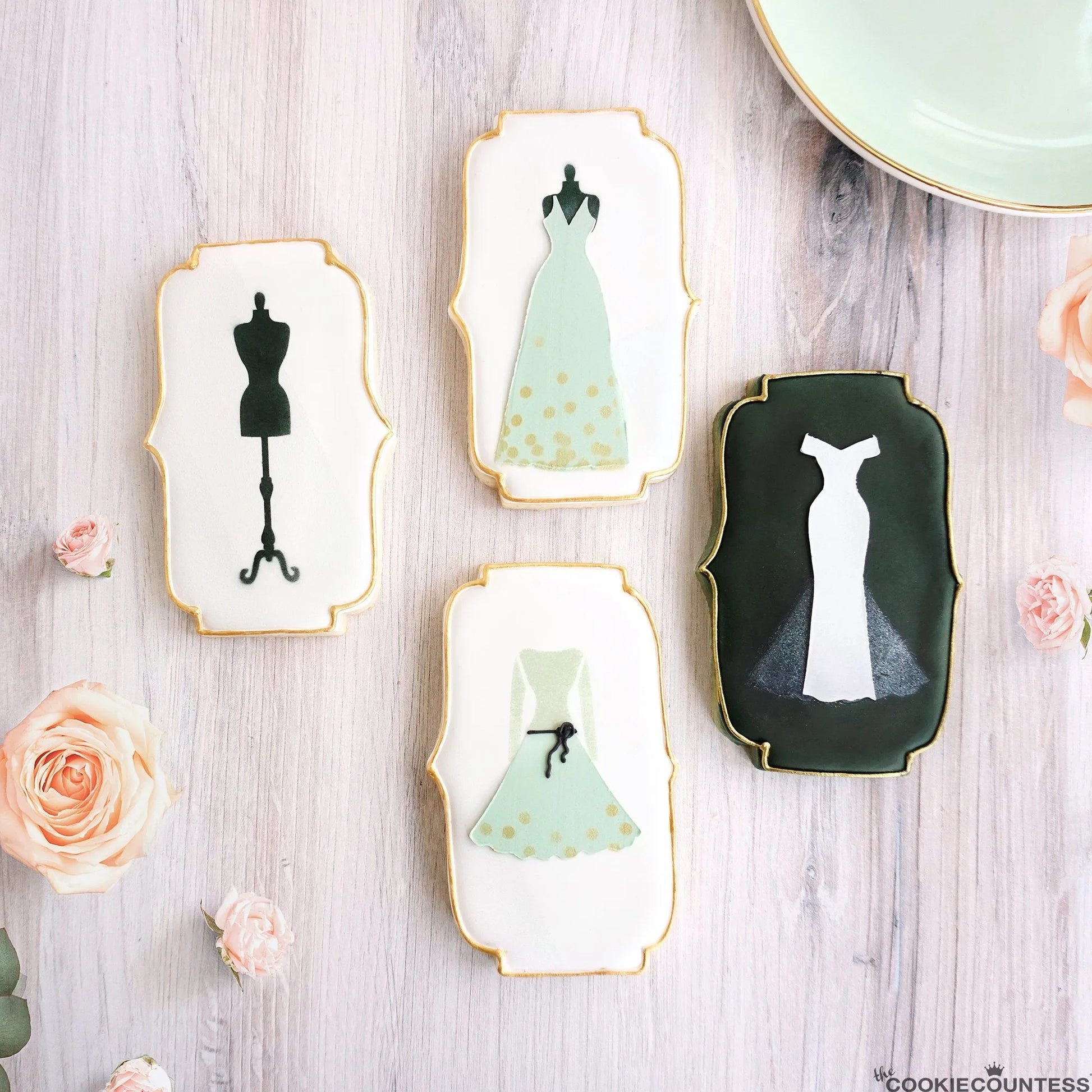 Sfeerbeeld van gedecoreerde koekjes met The Cookie Countess Wedding Dress Making stencil set, elegante koekjes met trouwjurken en paspop designs met gouden randen tussen roze rozen, perfect voor bruiloften en vrijgezellenfeesten