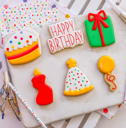 De zes Birthday workshopkoekjes naast elkaar: taart, Happy Birthday-bordje, groen cadeautje, rood kaarsje, feesthoedje en gele ballon