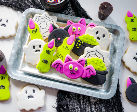 Halloween-koekjes met royal icing: spookjes, groene heksenvingers, zwarte kat, roze vleermuis, heksenketel en spinnenweb