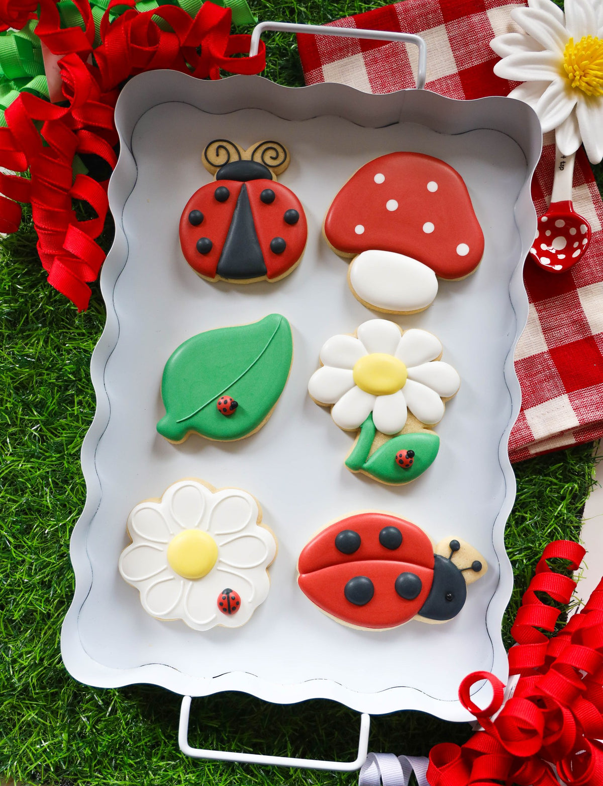 Zes Love Bug koekjes met royal icing op een wit dienblad: lieveheersbeestjes, madeliefjes, paddenstoel en blaadje