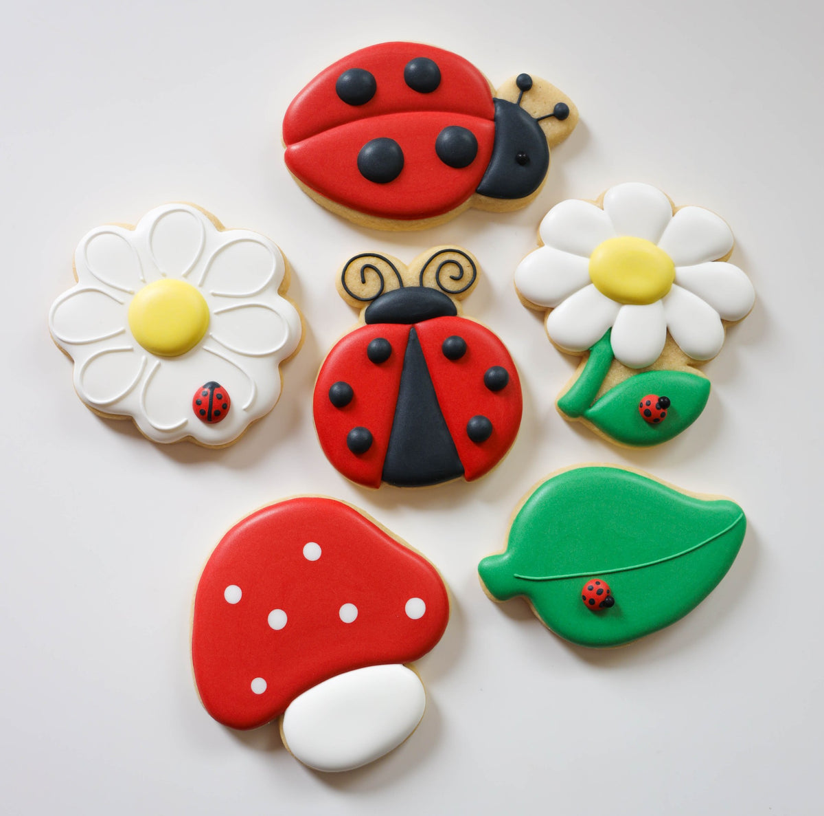 Close-up van de zes Love Bug workshopkoekjes: twee lieveheersbeestjes, twee madeliefjes, een paddenstoel en een blaadje