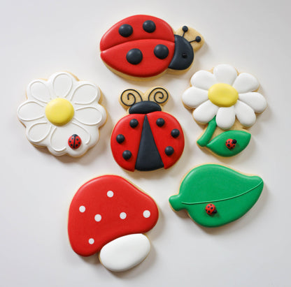 Close-up van de zes Love Bug workshopkoekjes: twee lieveheersbeestjes, twee madeliefjes, een paddenstoel en een blaadje